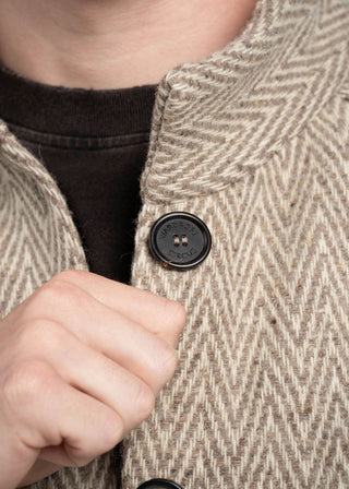 Close-up of a person wearing a textured beige coat with a button, focusing on the coat's pattern and texture.