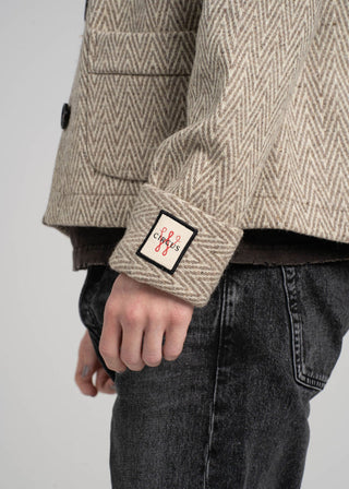 Close-up of a person wearing a textured jacket with a brand patch on a plain background