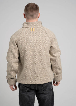 Man wearing a beige knitted sweater with a yellow label on a gray background