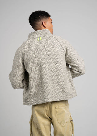 Person wearing a textured gray jacket with a brand logo on a plain background