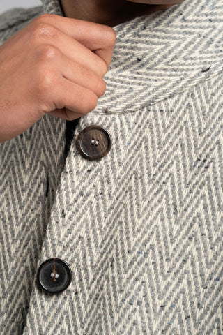 Close-up of a person buttoning a gray textured jacket with dark buttons.