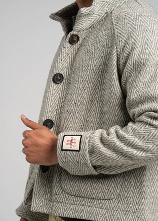 Close-up of a person wearing a textured jacket with a brand logo on the sleeve against a plain background