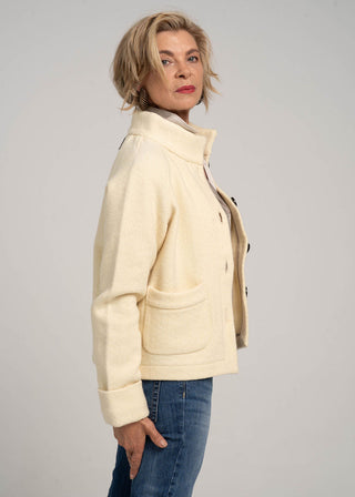 Woman wearing a cream-colored jacket and blue jeans against a gray background