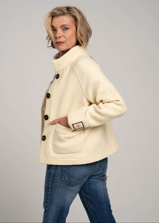 Woman wearing a cream-colored jacket with black buttons on a gray background