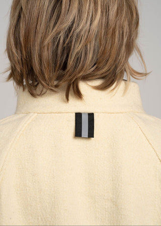 Back view of a person wearing a beige coat with a visible brand label on a plain background