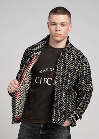 Man wearing a patterned jacket over a black t-shirt with visible text on a gray background