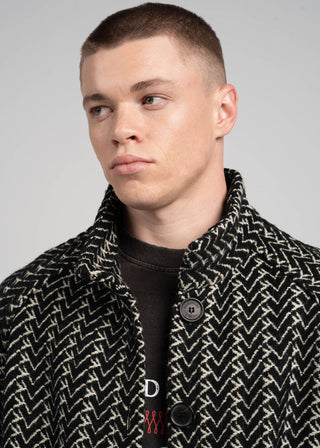 Man wearing a patterned coat with a brand logo on a gray background