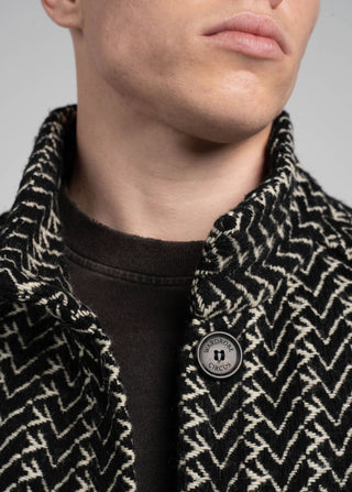 Close-up of a person wearing a patterned coat with a button, on a plain background