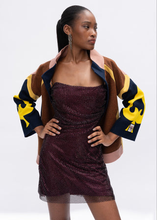 Woman wearing a maroon dress with a brown and yellow spade jacket on a white background