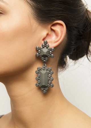 Close-up of a person wearing a pair of black 3D-printed earrings with a neutral background