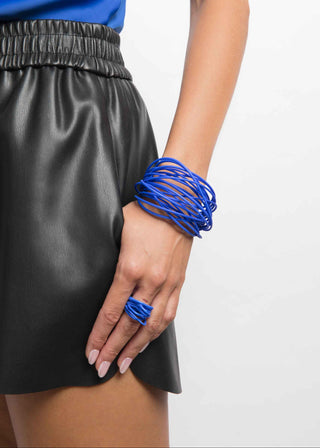 Person wearing a black skirt and blue top with multiple blue bracelets on a white background