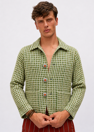 A man wearing a green and white checkered long-sleeve button-up shirt with decorative red and green buttons, paired with red striped trousers, against a plain light gray background.