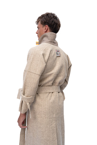 A man shown from the back wearing a high-neck, belted beige coat or robe against a plain white studio background.