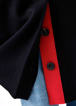 Close-up of a black coat or jacket with a bold red inner panel and black buttons, worn over light blue denim.