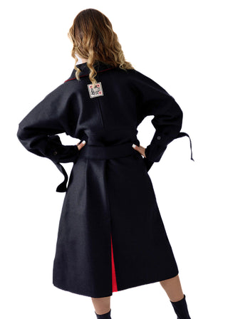 A model shown from the back wearing a long black coat with a red side panel and a small patch on the back collar, set against a plain white background.