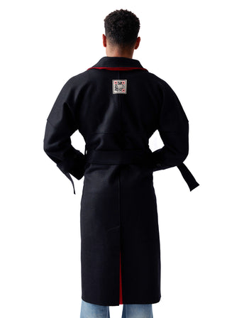 A man viewed from the back wearing a long black robe with a waist tie and red piping trim along the collar and inner front opening. A small square patch is visible on the upper back.