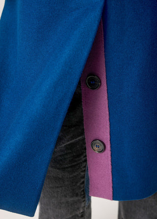 Close-up of a blue wool-blend blazer with a contrasting magenta inner placket and dark buttons, worn over dark gray jeans.