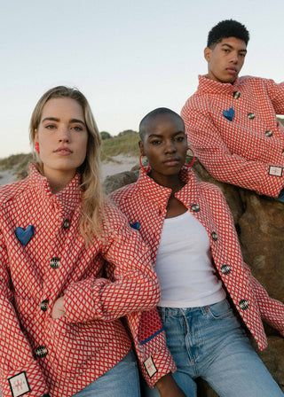 Three people wearing red checkered jackets with heart and star buttons on a beach.