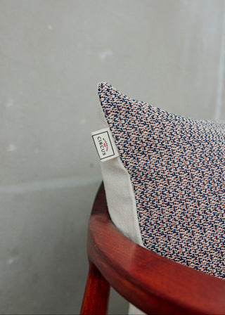 Textured pillow with a brand label on a wooden chair against a gray background