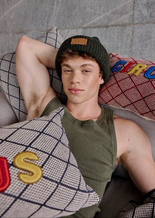 Person wearing a green tank top and beanie lying on a couch with colorful pillows.