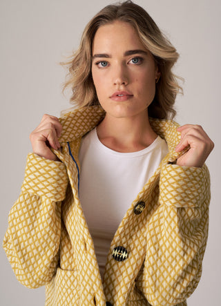 Woman wearing a yellow patterned coat against a neutral background
