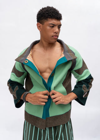 A model wearing a color-blocked knit zip-up cardigan with sage green, teal, and brown panels, shown against a plain light gray studio background.