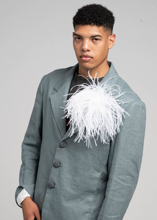 Person wearing a gray coat with a unique white feathered accessory on a plain background